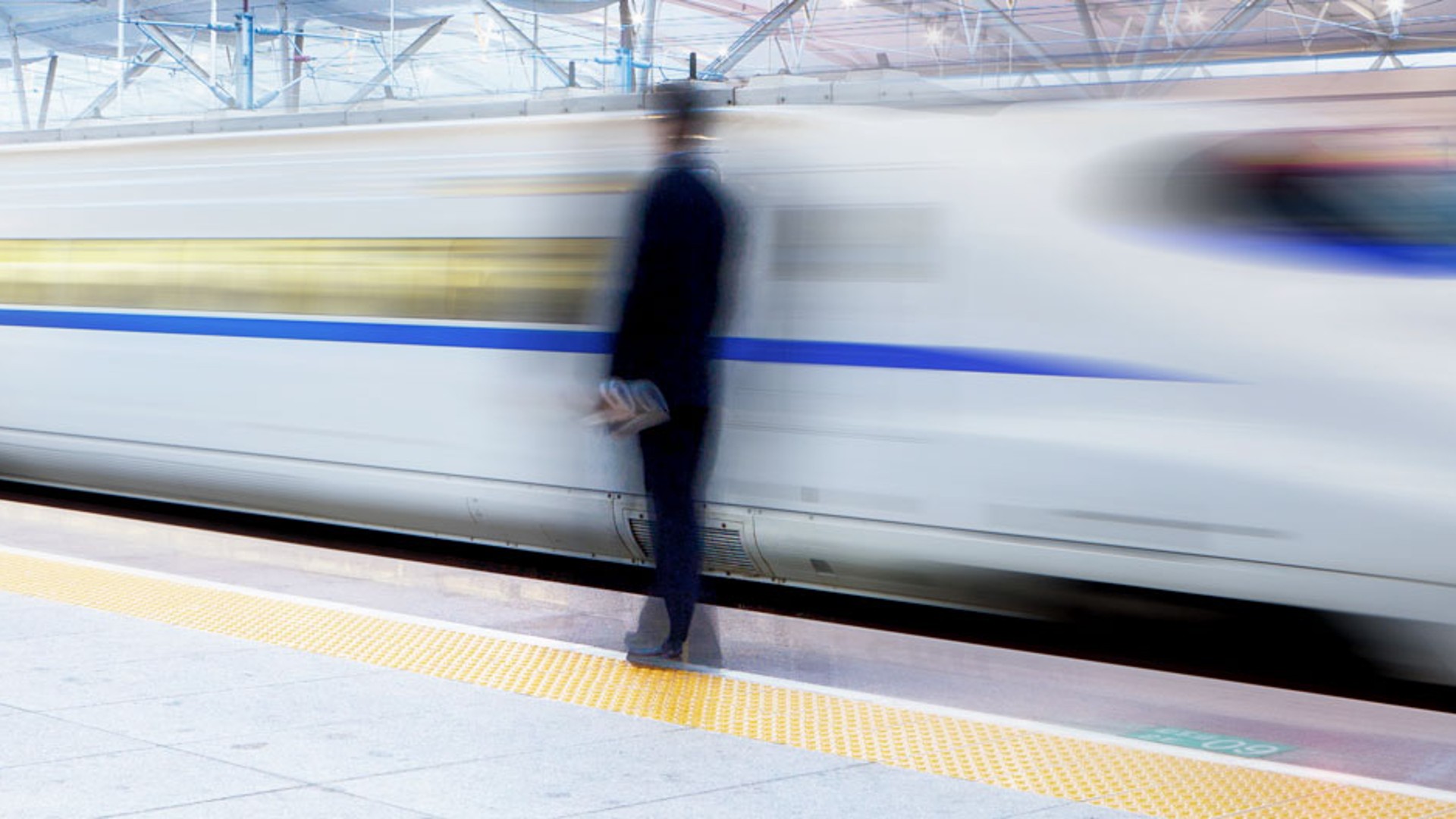 White fast train driving past a passenger at a train station