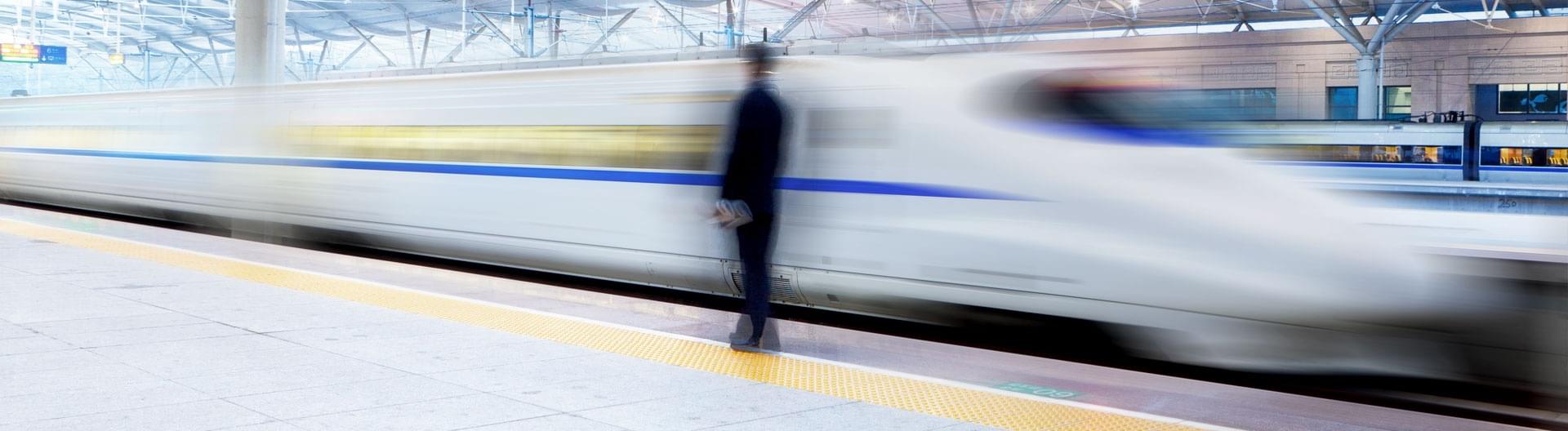 Weißer Schnellzug fährt an Passagier der am Bahnsteig steht vorbei