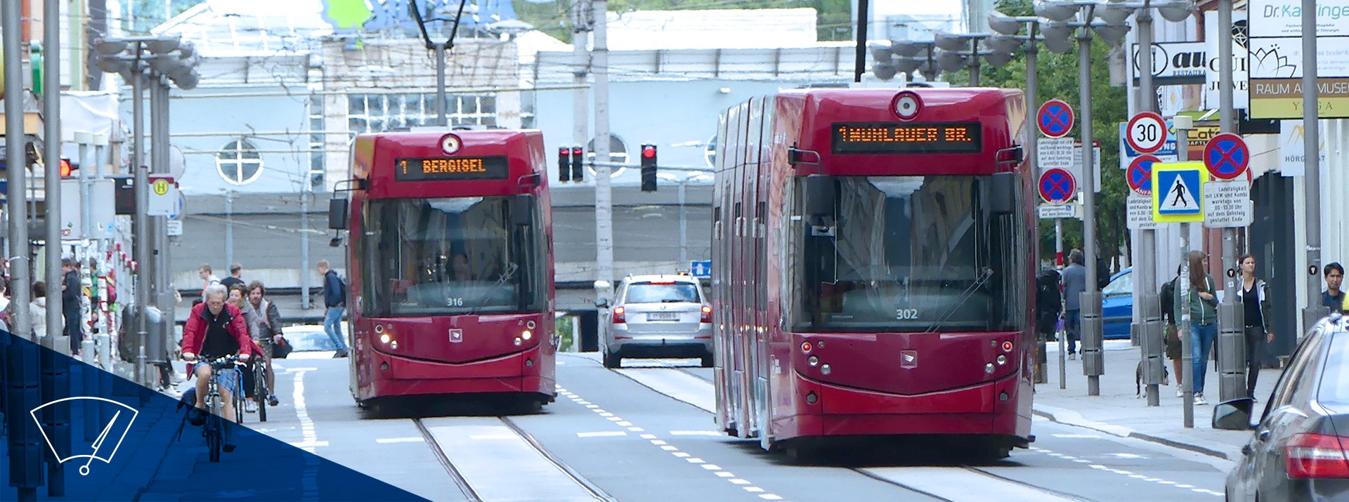 Zwei rote Straßenbahnen in urbaner Umgebung.