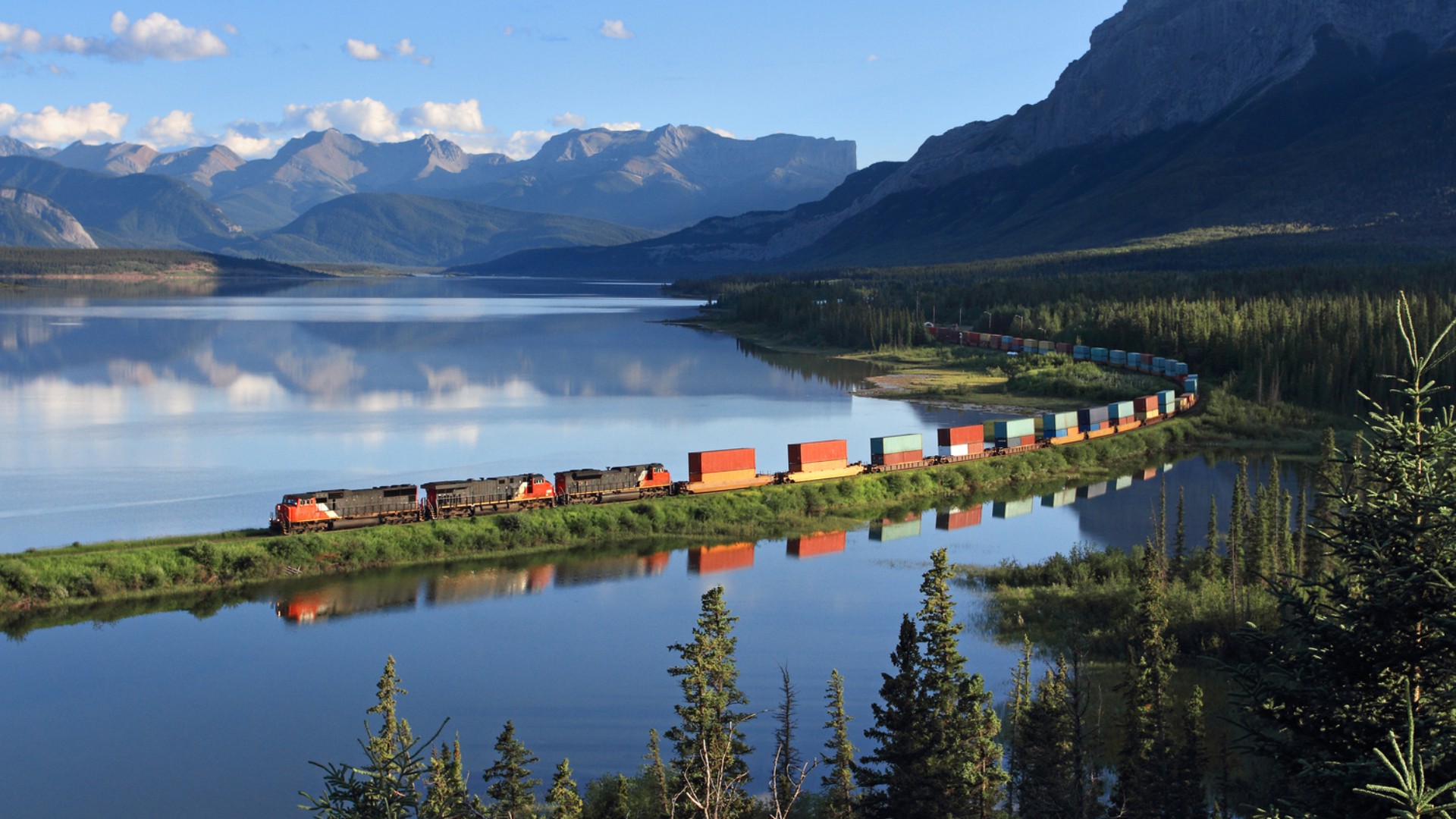 Train traveling through mountainous landscape by lake.