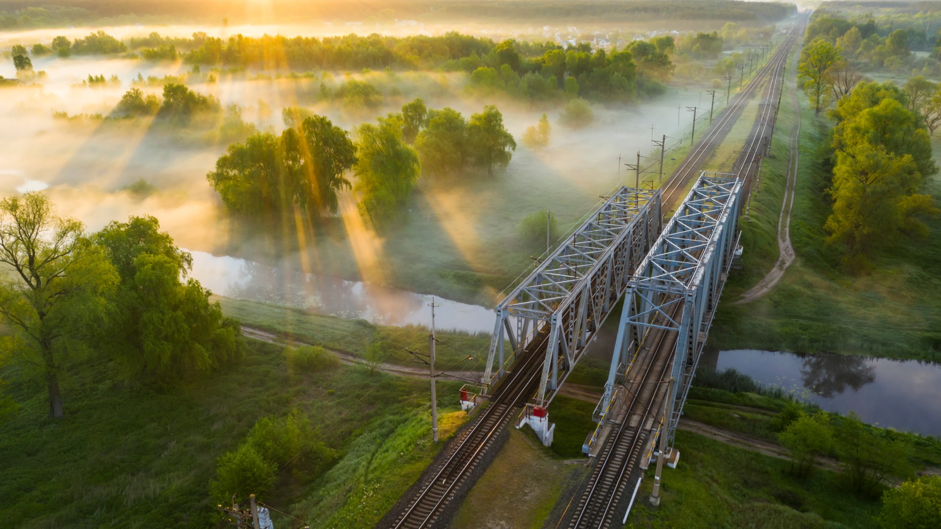Green landscape with a bridge across a river and two rail tracks