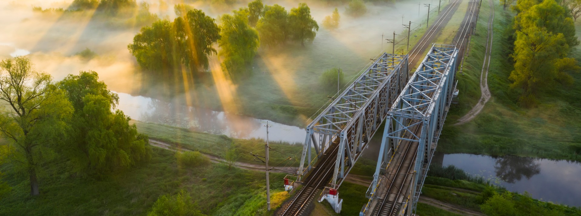 Green landscape with a bridge across a river and two rail tracks