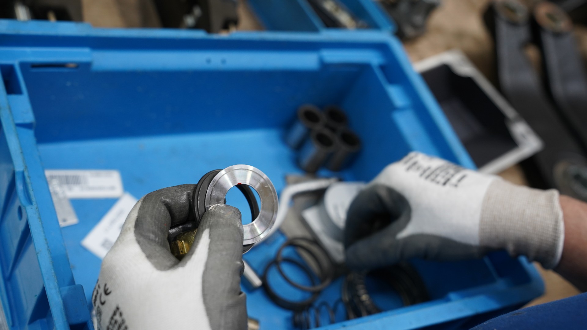 Hands holding metal component over blue toolbox.