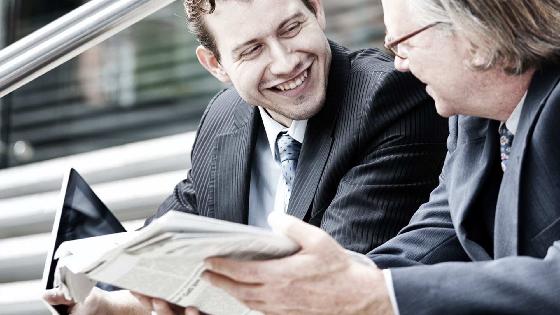 Businessmen discussing while reading newspaper and tablet.