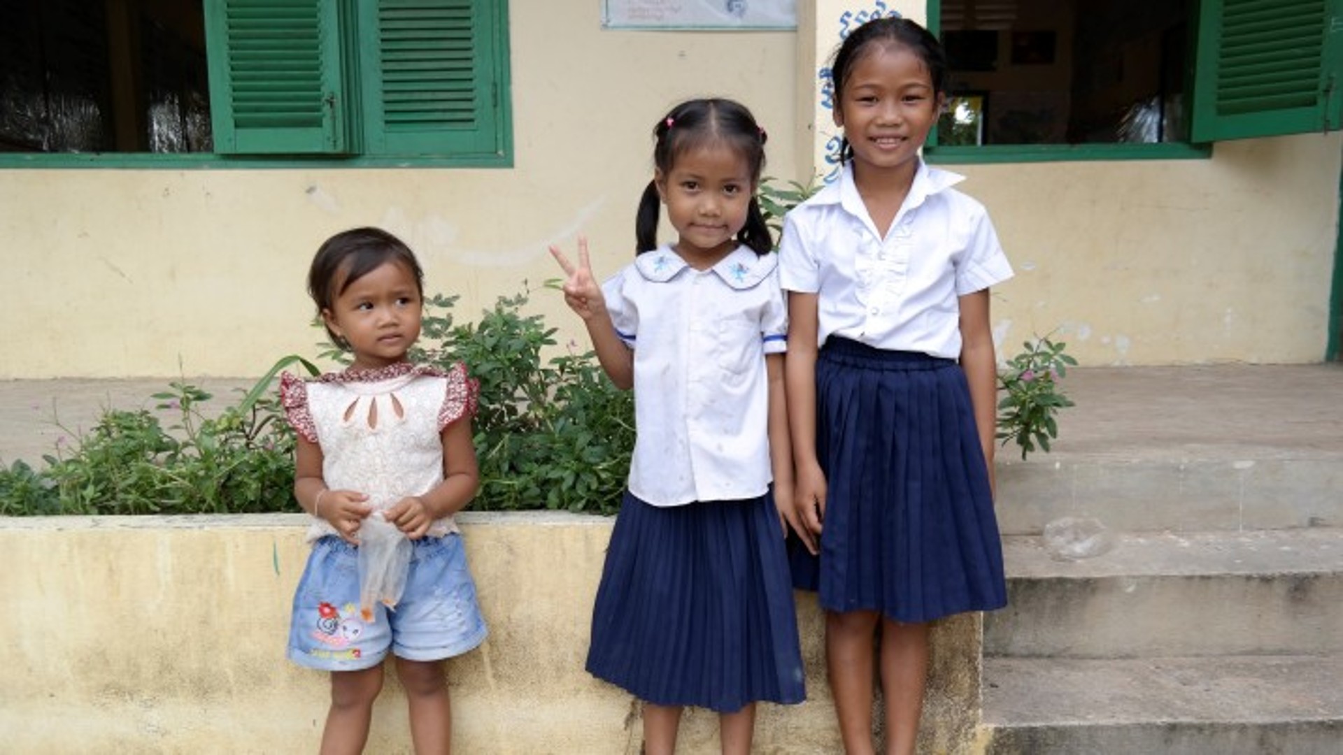 Three schoolgirls posing outside a classroom.