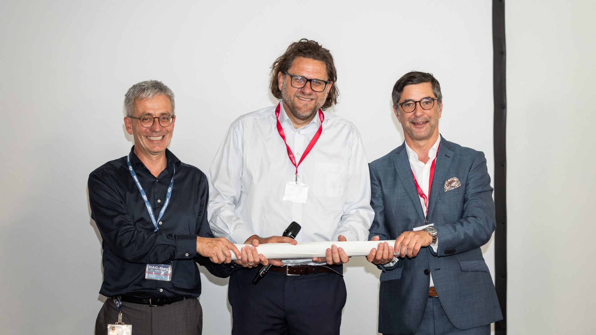 Three men holding a document on stage.