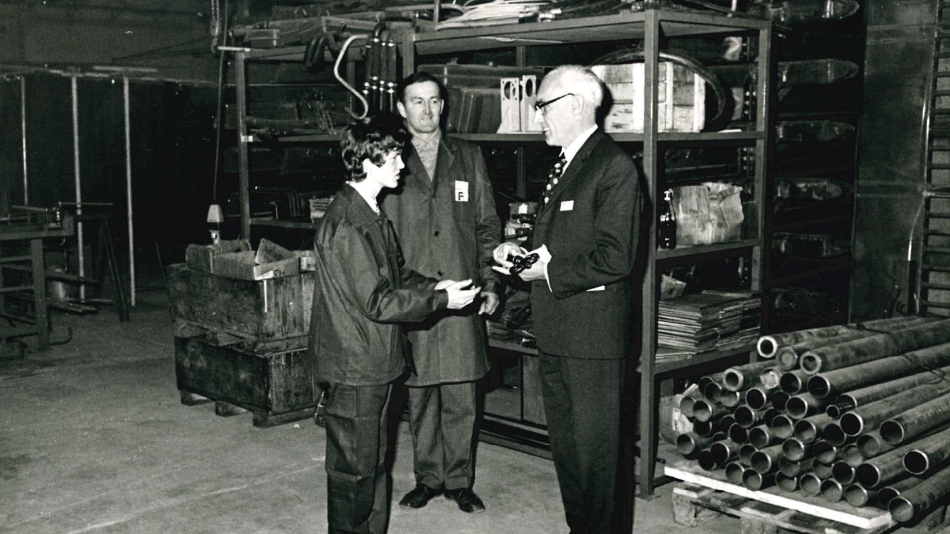 Three men engaging in discussion in workshop.