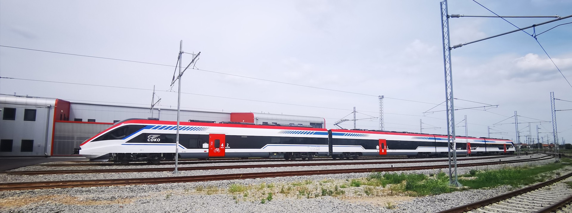 Modern train on tracks near industrial facility.