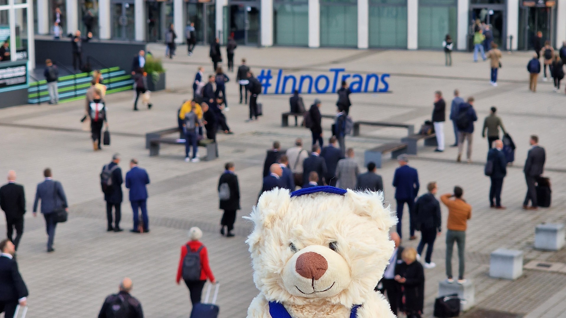 Teddy auf Geländer vor InnoTrans 2022 Messebesuchern.