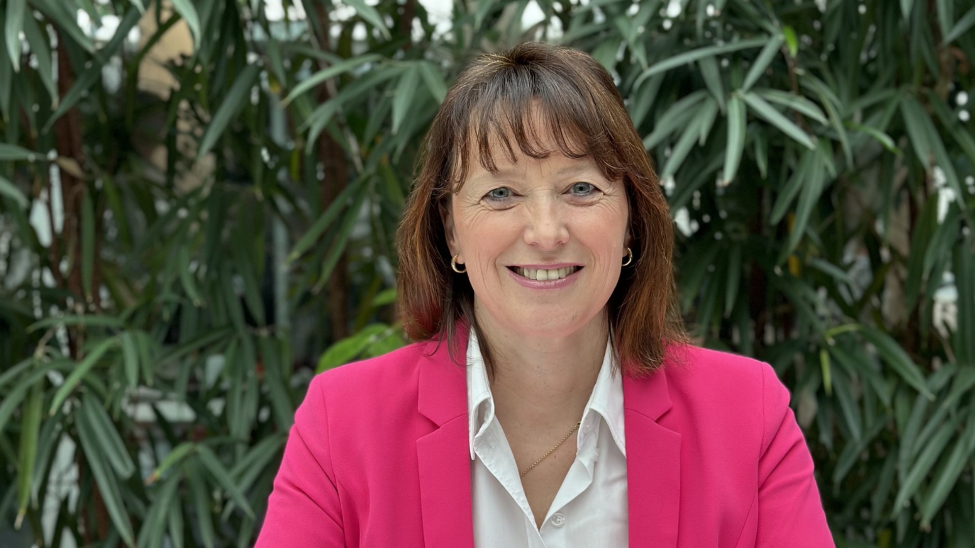 Woman in pink blazer smiling among greenery.