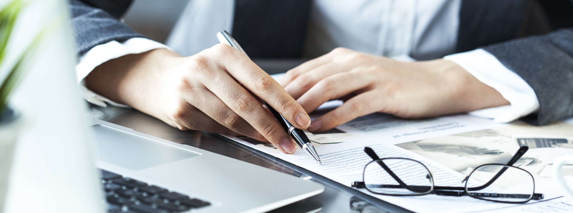Hands writing notes on documents with laptop.