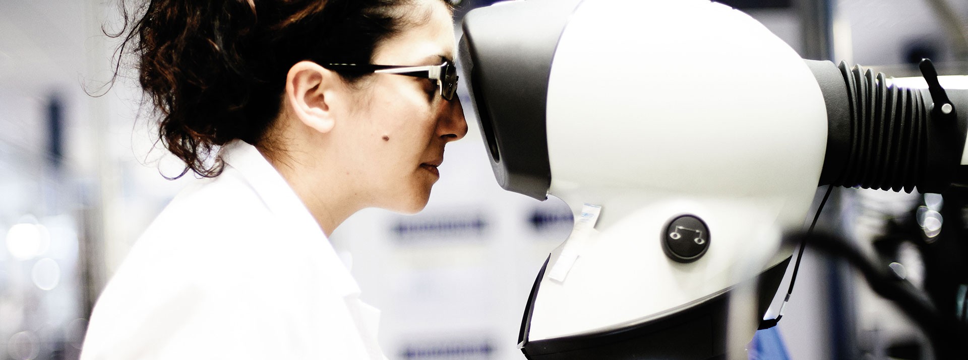 Woman examining equipment through a microscope lens.