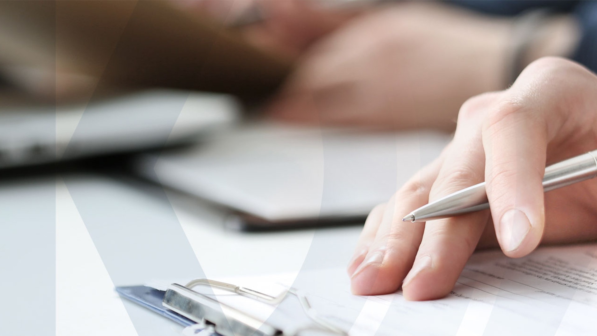 Hand mit Stift über Dokumenten auf Tisch.