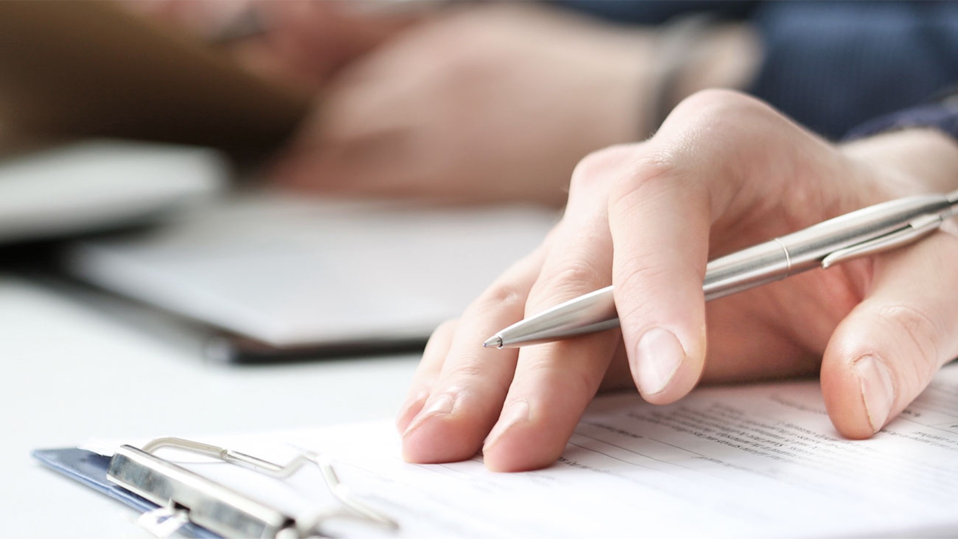Hand holding pen over document on desk.