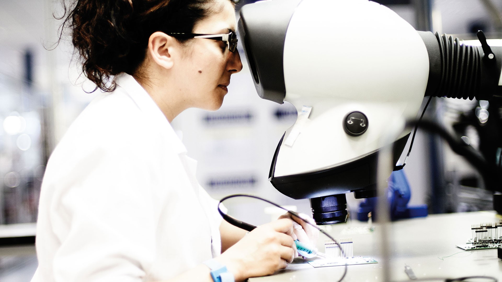 Woman inspecting circuitry under microscope.