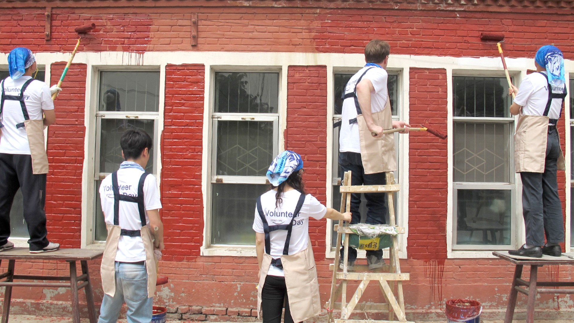 Volunteers painting a brick wall red.