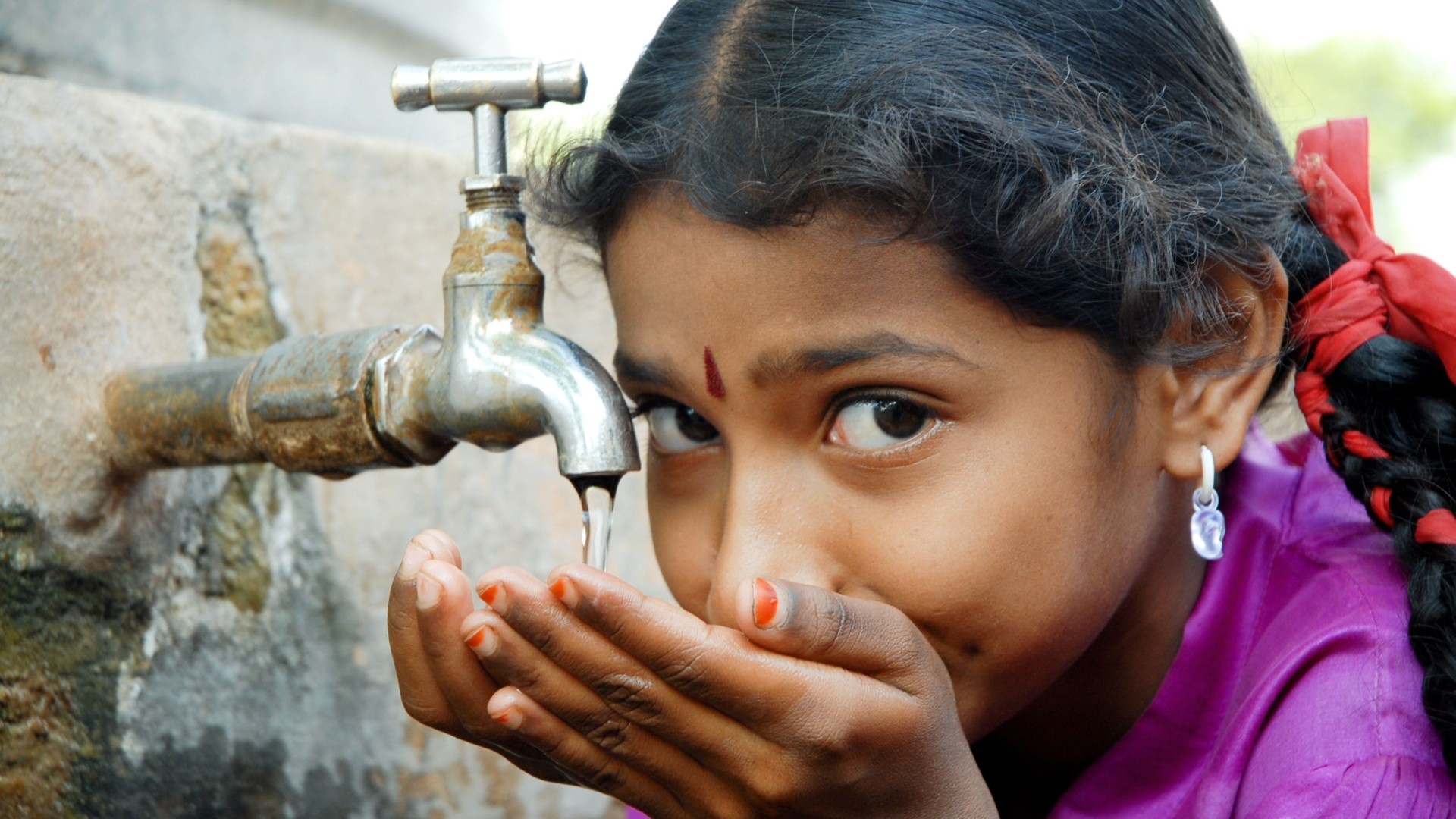 Girl drinking water from a public faucet.