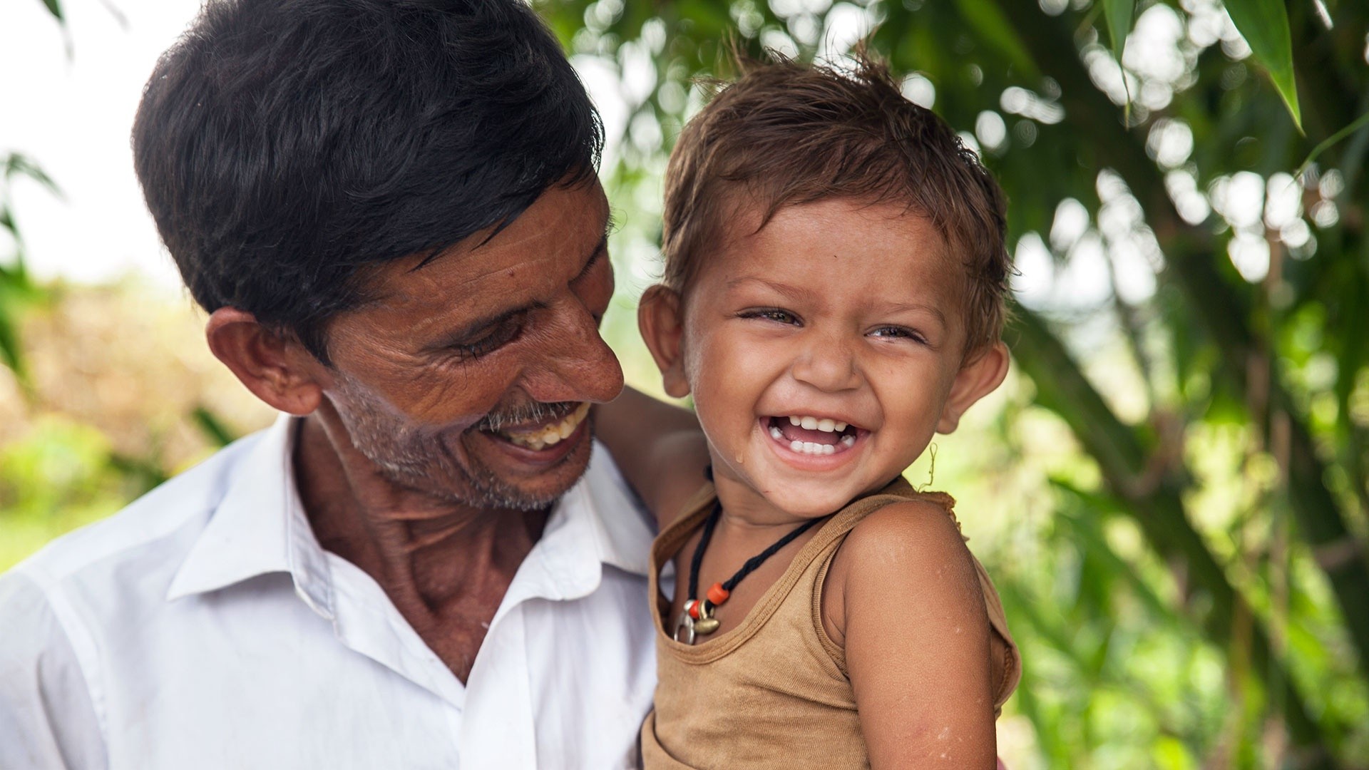 Laughing child with adult in green environment.