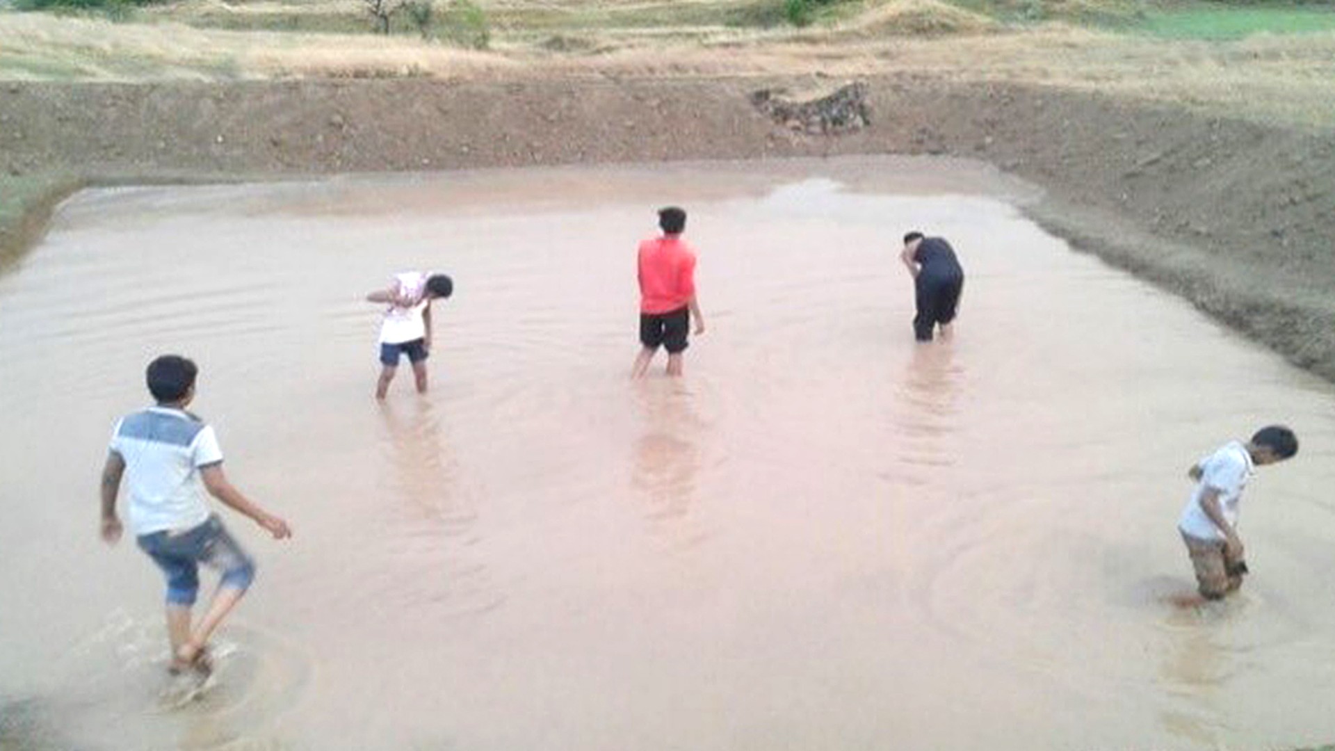 Children playing in muddy water-filled area.