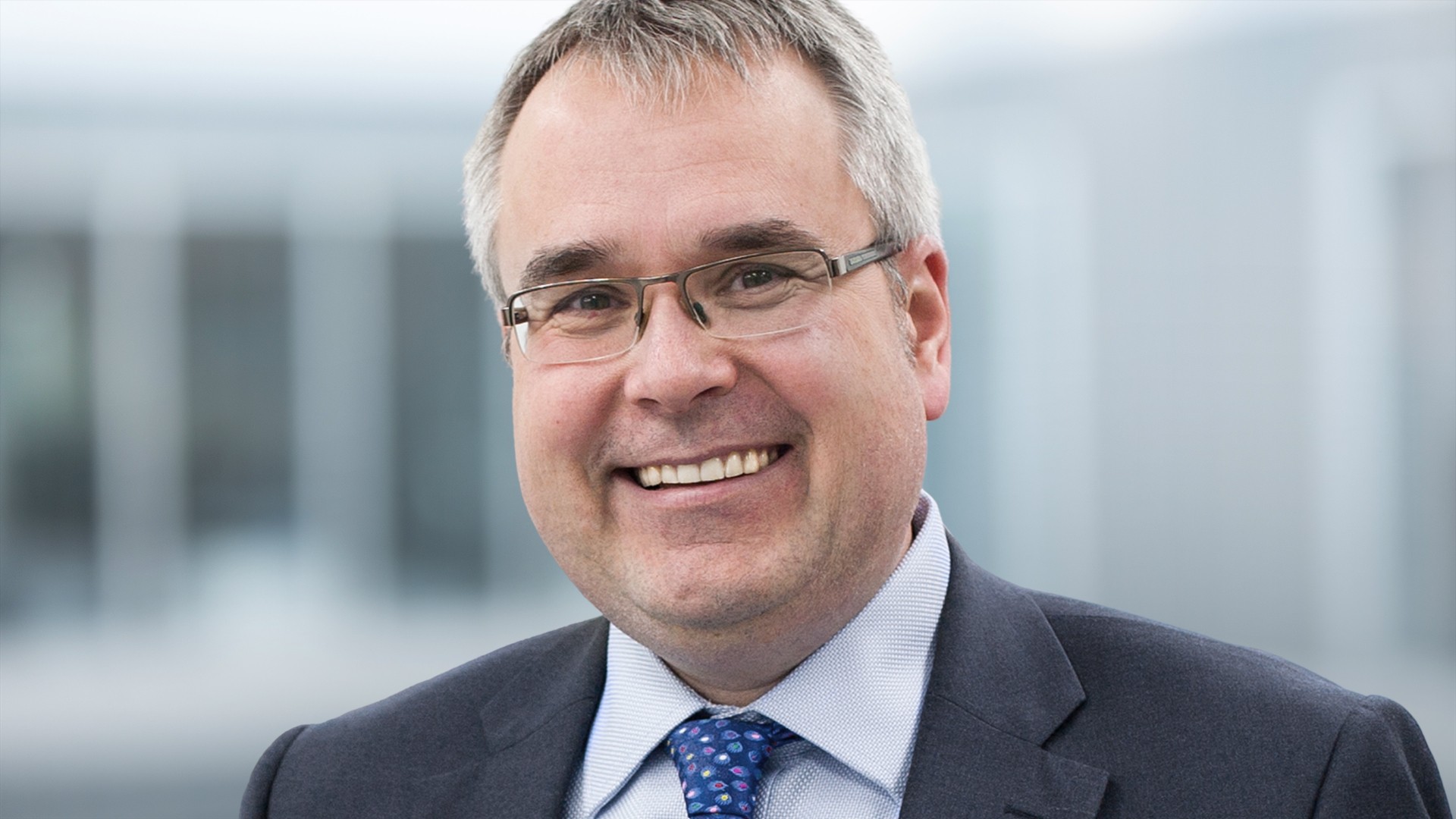 Smiling man in business attire, blurred background.